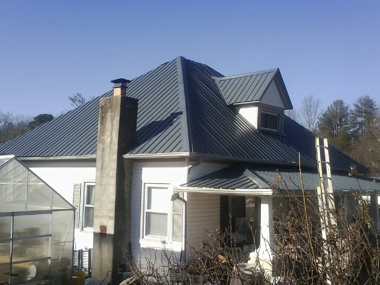 Dark blue standing seam metal roof on a white farmhouse with dormer — Slate & Tile Roof Repair by Roofing Brothers in Condon