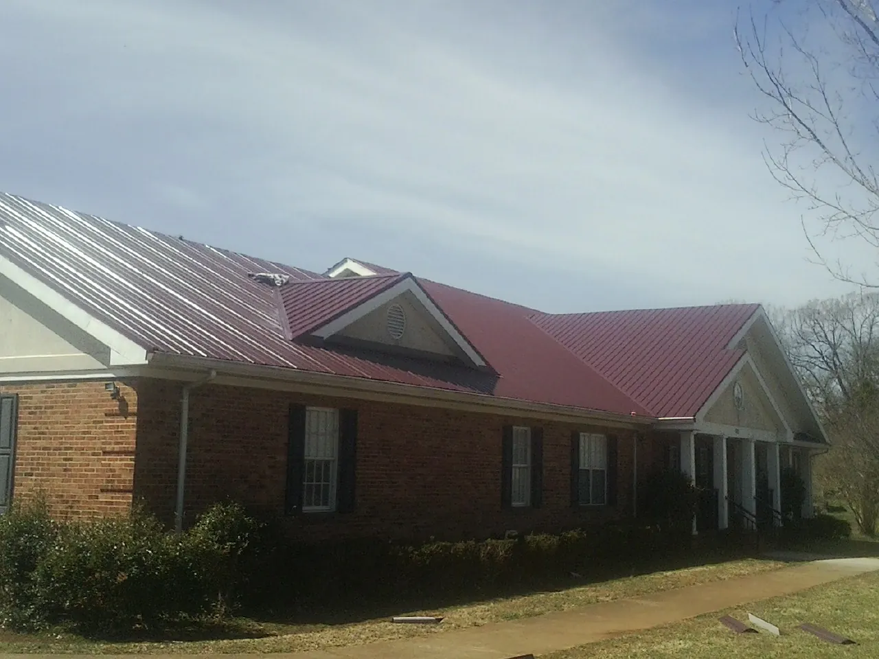 Red metal roof with gabled entries on a long brick building, from a Hail Damage Roof Repair job in Condon