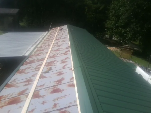 Old rusted panels beside newly installed green metal roofing — Wind Damage Roof Repair by Roofing Brothers in Condon