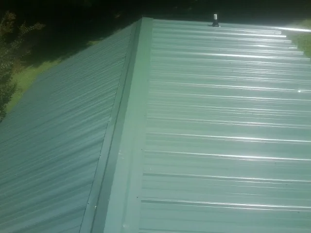 New green metal panels meeting at the ridge of a roof — Flat Roof Repair work by our crew in Condon