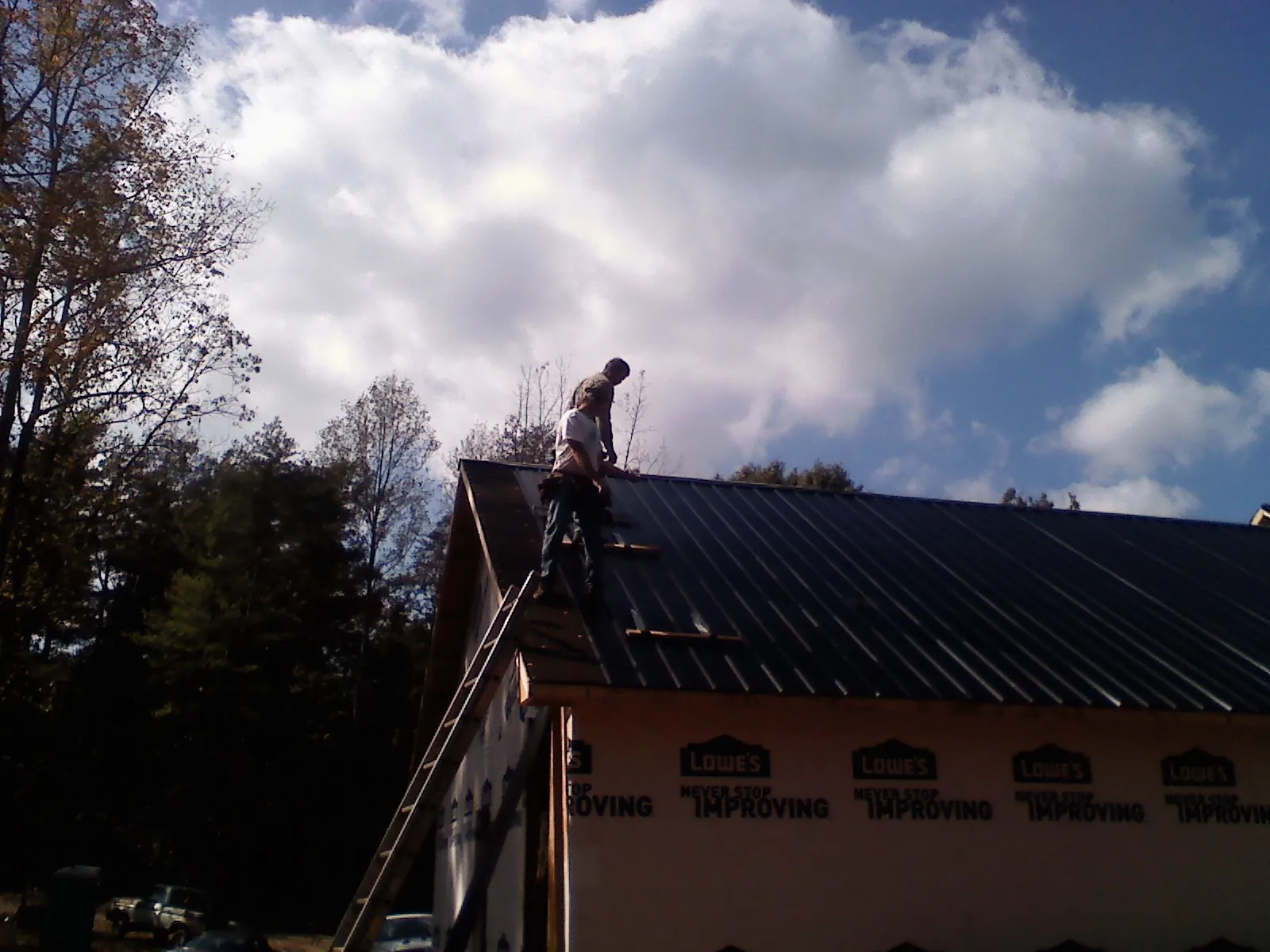 Roofer fastening dark metal panels high against a cloudy sky, from a Roof Inspection job in Condon