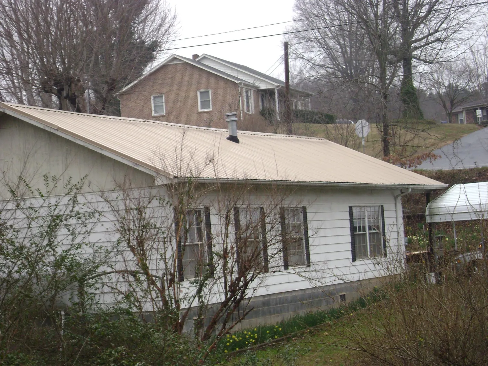 Tan metal roof on a white sided house set into a hillside — Commercial Roofing by Roofing Brothers in Condon